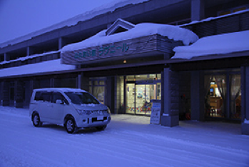 雪景色の邸宅の前に止まっている白いクルマ